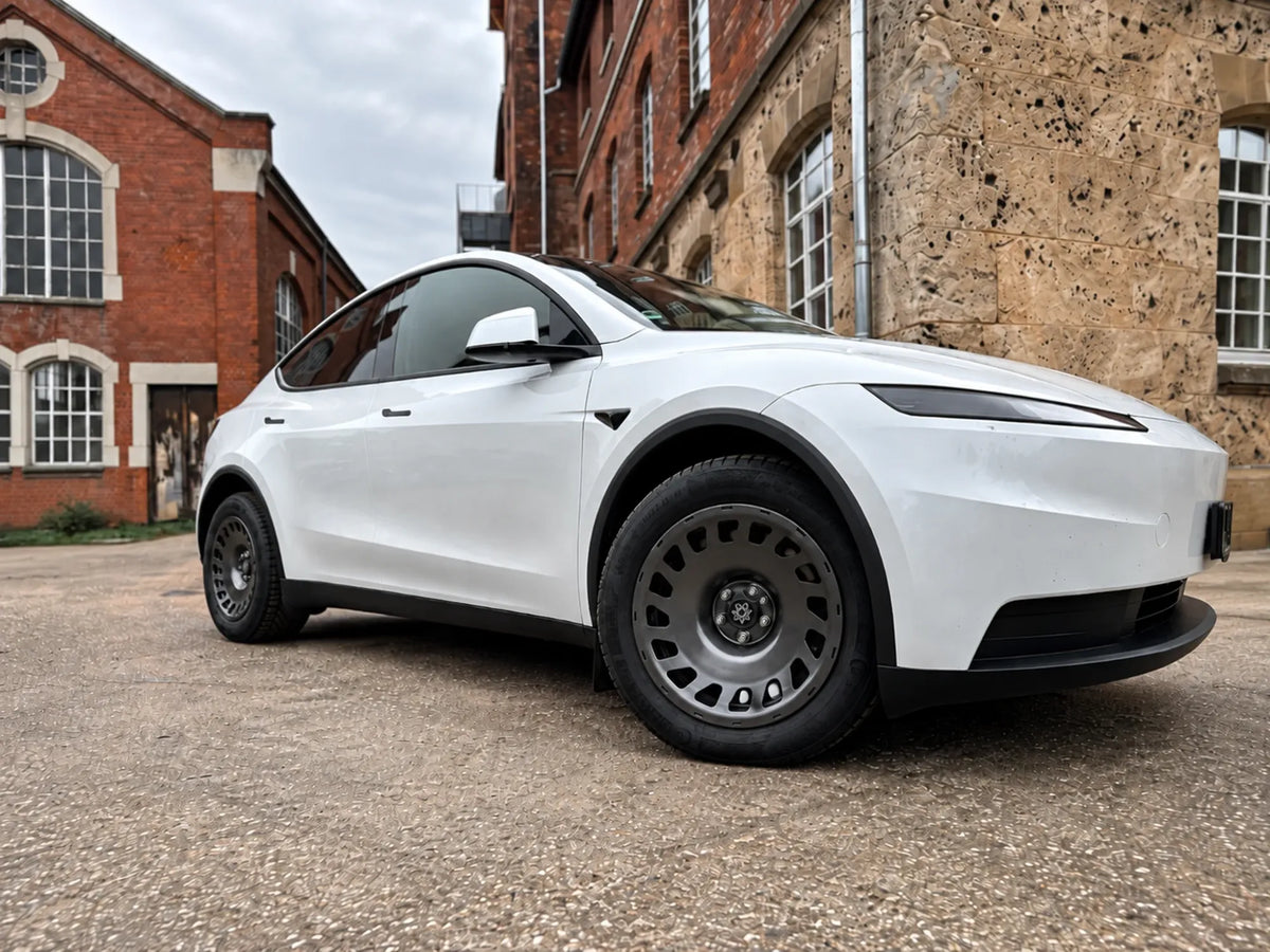 Weißes Tesla Model Y Juniper mit Erion 10 Kompletträdern 18 Zoll in Chrome Shadow Grey vor historischem Backsteingebäude