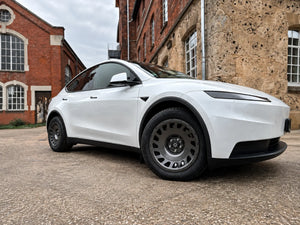Weißes Tesla Model Y Juniper mit Erion 10 Kompletträdern 18 Zoll in Chrome Shadow Grey vor historischem Backsteingebäude