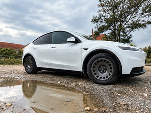 Tesla Model Y Juniper mit Erion 10 Chrome Shadow Grey 18 Zoll auf Schotter mit Spiegelung in der Pfütze